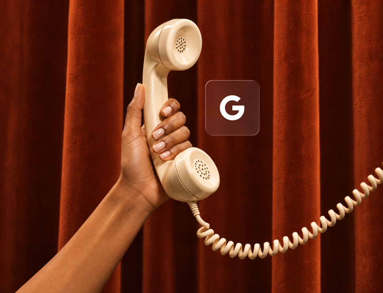 A hand holds a cream telephone receiver against a red velvet curtain, next to the Google G.