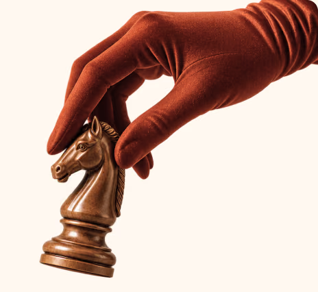 A hand in a long rust satin glove lifting a bronze chess knight.
