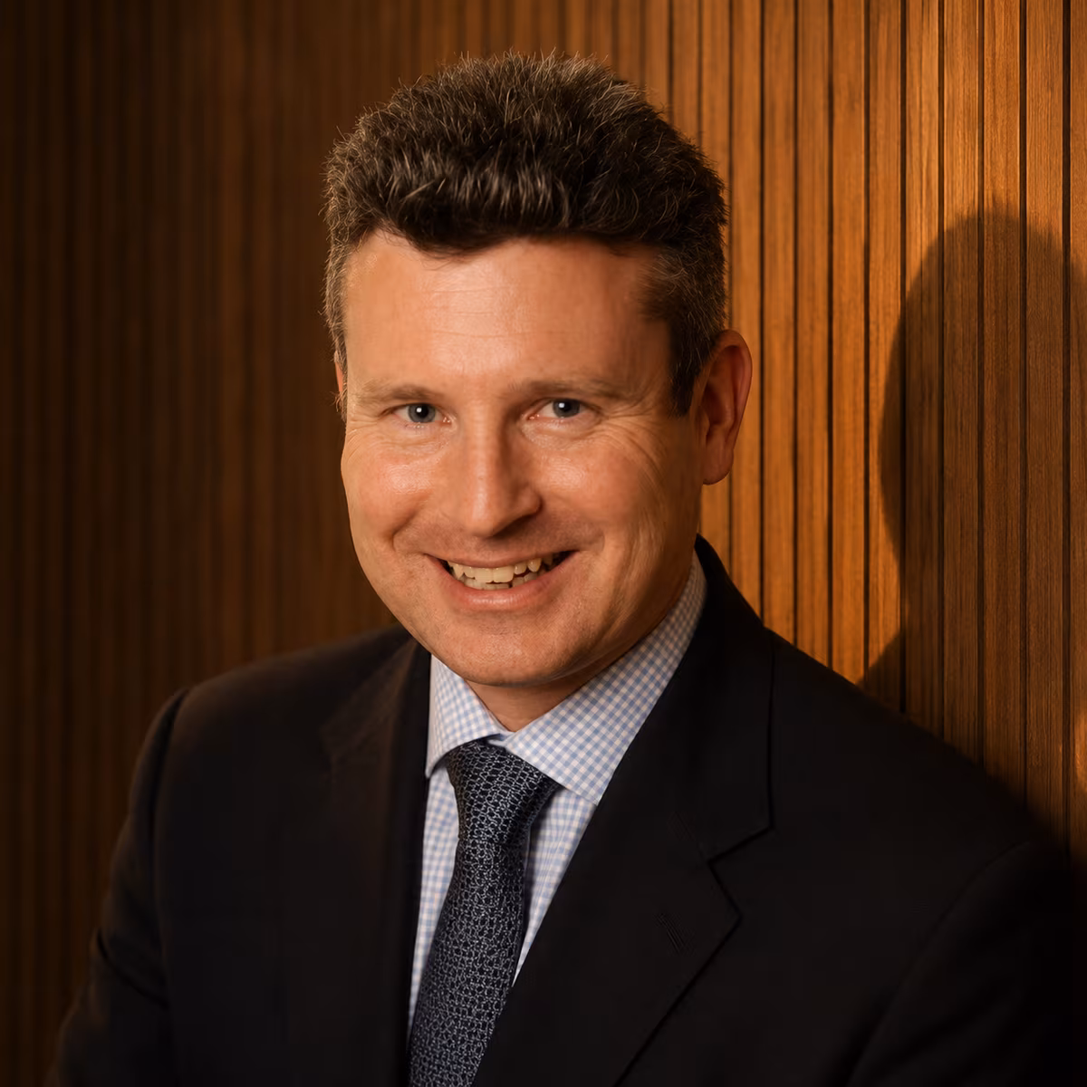 Euan Campbell of Quicken, smiling, in a dark suit and tie against a wood-panelled wall.